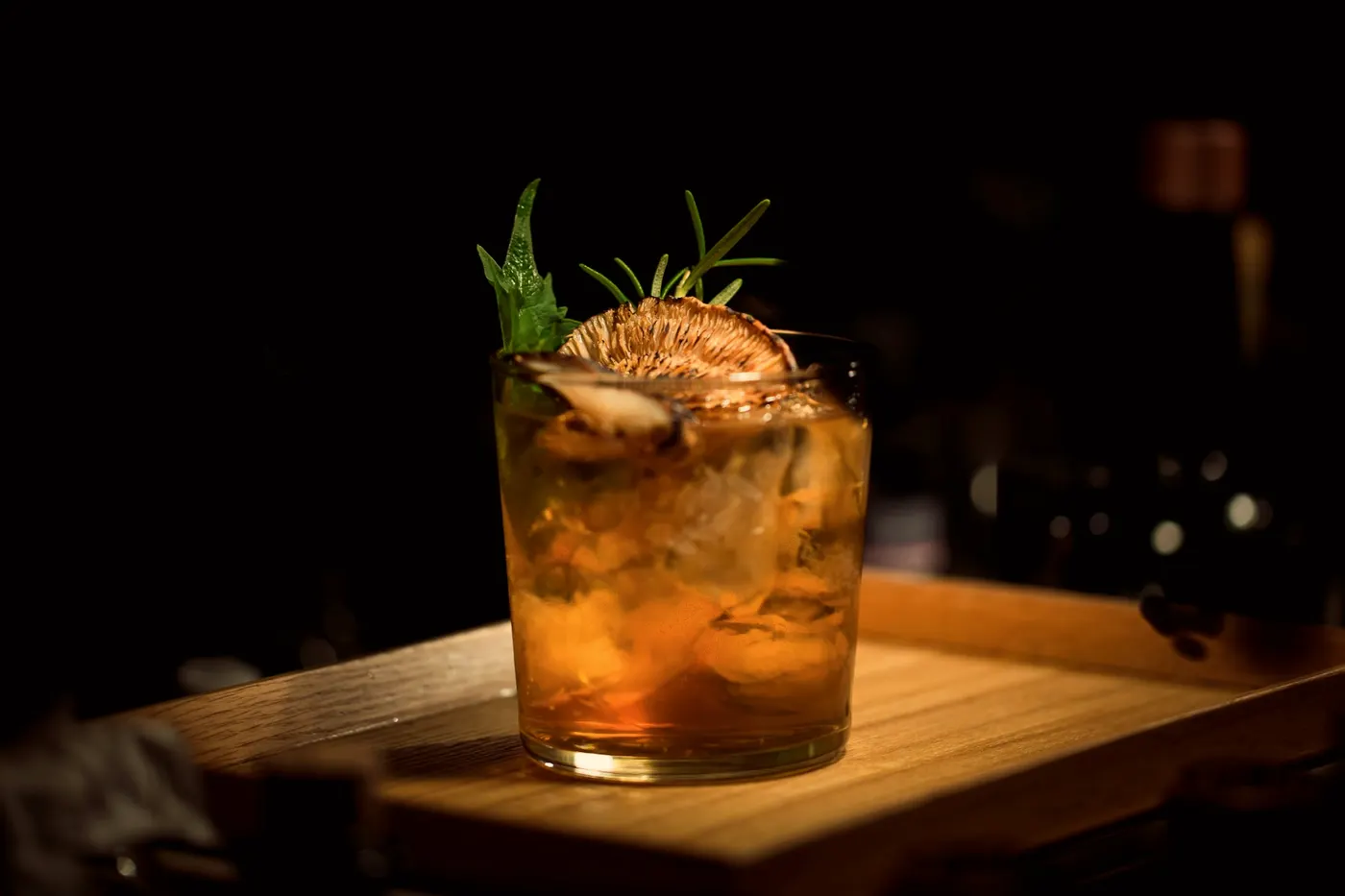 A smoked cocktail with herbs on a dark bar
